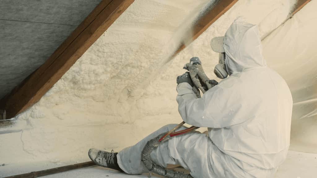 VR Insulation technician applying spray foam insulation in an attic